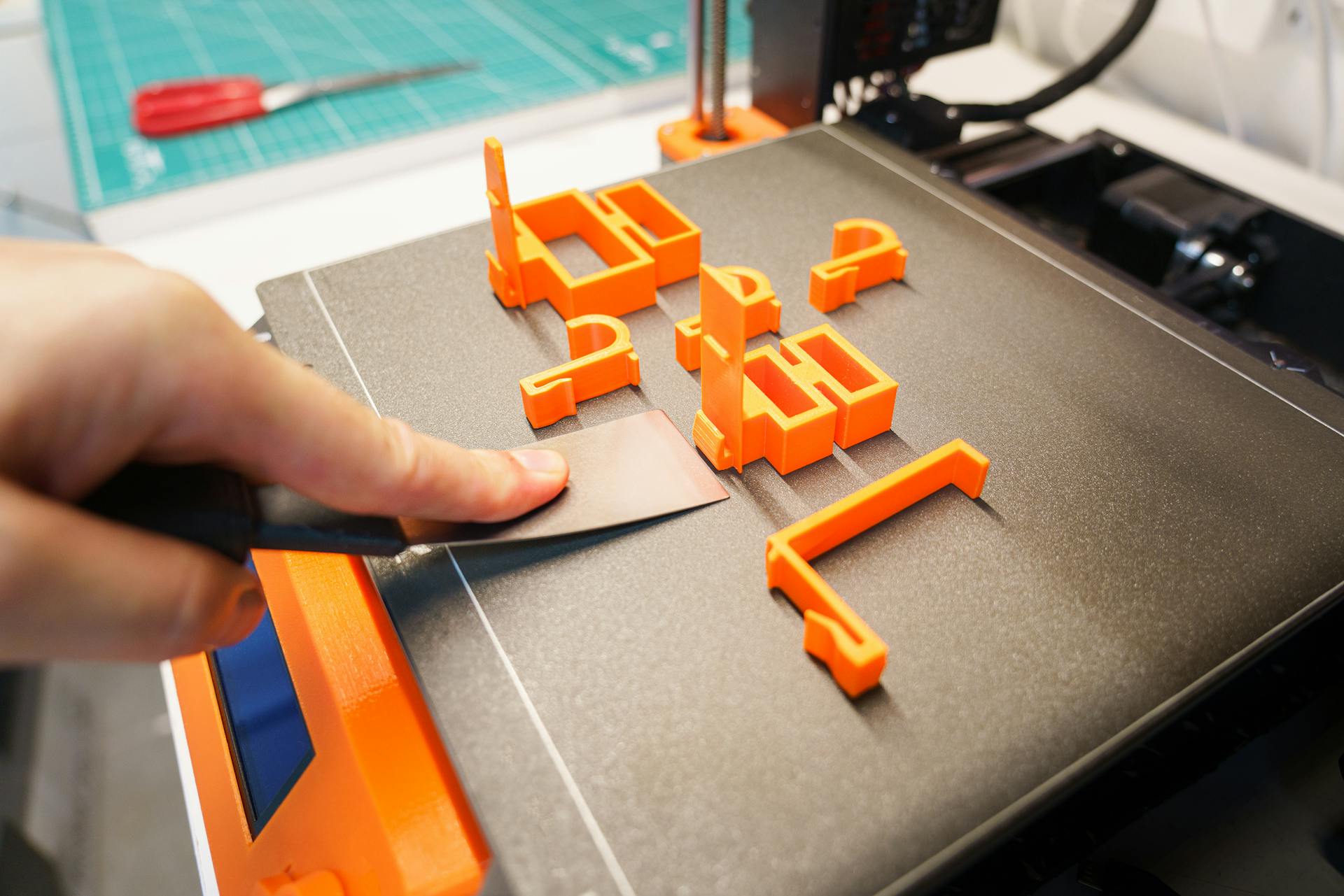 3D printer making orange parts in a small workshop